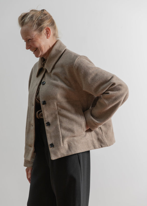 Person wearing a beige coat against a plain background