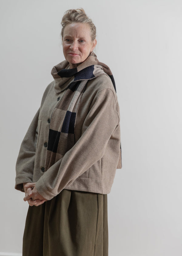 Person wearing a beige coat and plaid scarf against a plain background