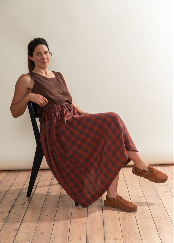 Woman sitting on a chair wearing a long, patterned dress in a room with wooden flooring.