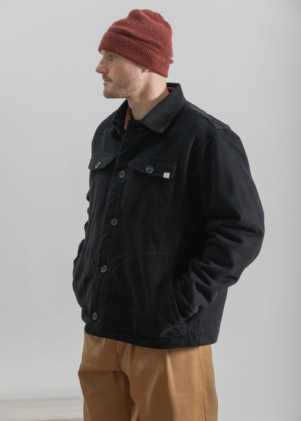 Man wearing a black jacket, red beanie, and brown pants against a plain background