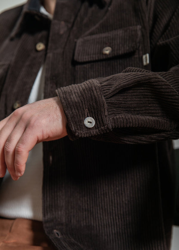 Close-up of a person wearing a brown corduroy jacket with a buttoned sleeve.