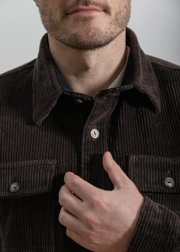 Man wearing a brown corduroy jacket with a neutral background