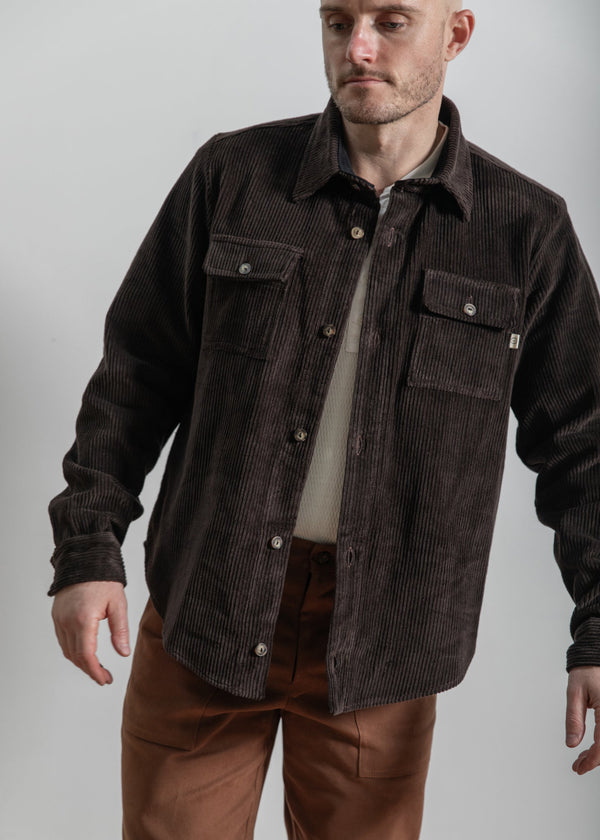 Man wearing a brown corduroy shirt over a beige shirt with a plain background