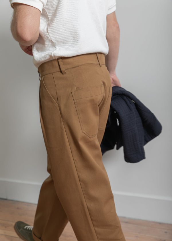 Person wearing brown pants and a white shirt, holding a dark jacket against a plain background