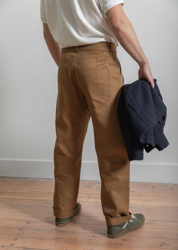 Person wearing brown pants holding a dark jacket on a wooden floor.
