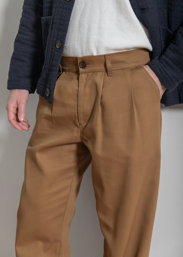 Brown pleated pants worn by a person against a neutral background