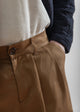 Close-up of brown pants with a button, worn by a person, on a plain background