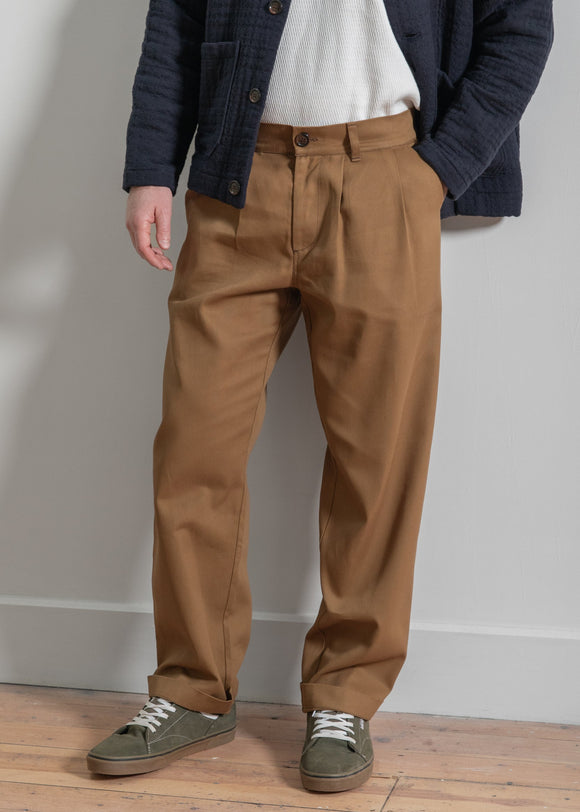 Person wearing brown pants and a navy jacket on a wooden floor with a white wall background