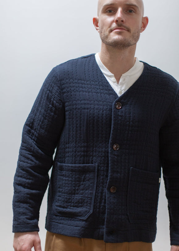 Man wearing a navy textured cardigan over a white shirt against a plain background