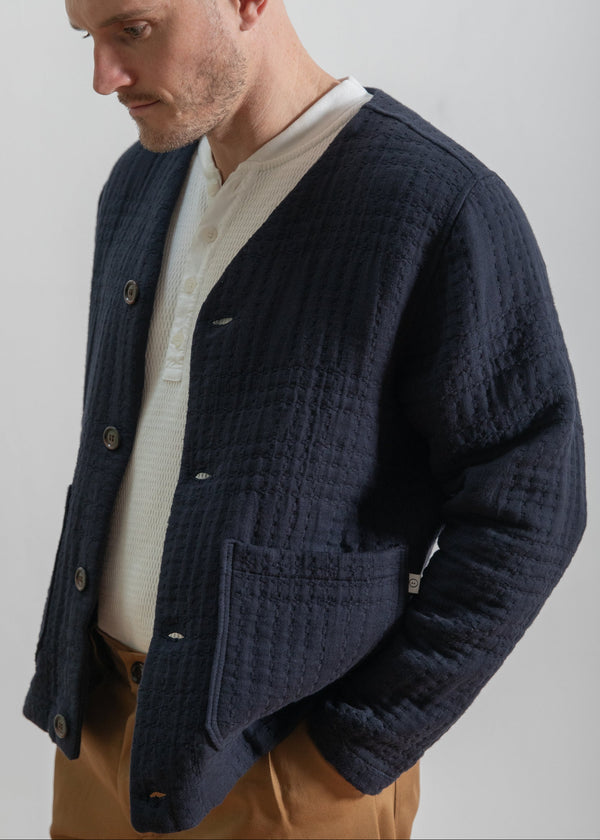 Man wearing a navy textured cardigan over a white shirt with a plain background