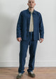 Person wearing a blue jacket and pants standing on a wooden floor with a white wall background