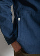 Close-up of a person wearing a blue denim jacket with a visible brand logo on a plain background