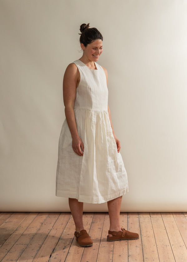 Woman wearing a white dress standing against a plain wall.