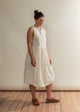 Woman wearing a white dress standing against a plain wall.