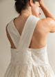 Woman wearing a white dress with a V-neck and button details, standing against a neutral background.