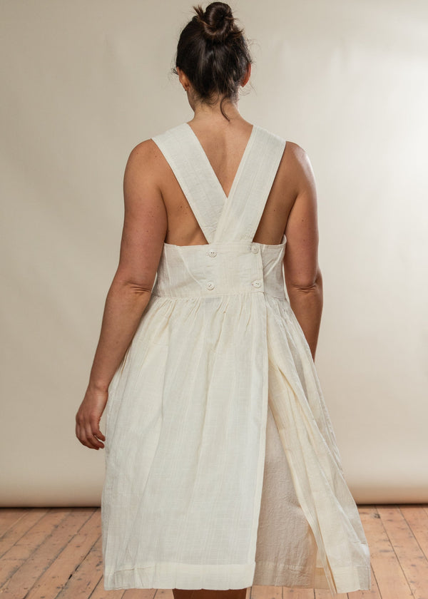 Woman wearing a white dress with a V-neck and criss-cross back on a plain background