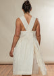 Woman wearing a white dress with a V-neck and criss-cross back on a plain background