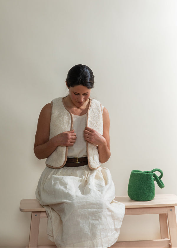 Woman sitting on a bench wearing a white dress with a green bag beside her.
