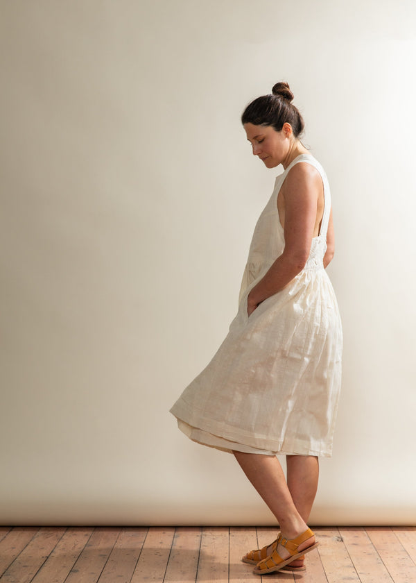 Woman wearing a white dress standing against a plain wall.
