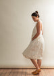 Woman wearing a white dress standing against a plain wall.