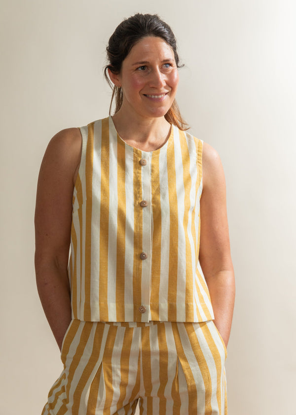 Woman wearing a yellow and white striped sleeveless top and pants against a plain background