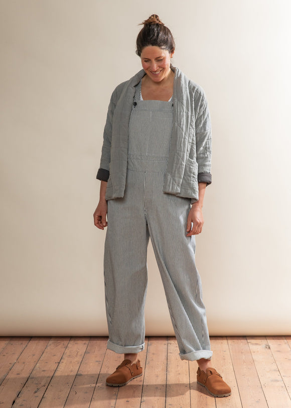 Woman wearing a gray outfit with a jacket and overalls on a wooden floor.