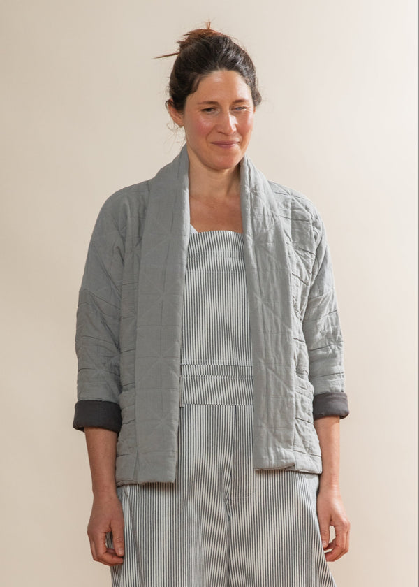 Woman wearing a light gray quilted jacket over a striped dress against a plain background
