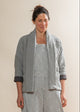 Woman wearing a light gray quilted jacket over a striped dress against a plain background