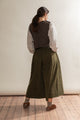 Person wearing a vest, shirt, and wide-leg pants standing against a plain wall.