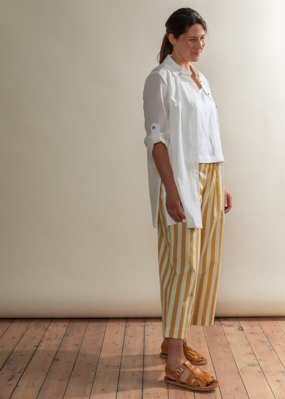 Woman wearing a white shirt and yellow striped pants standing against a plain wall.