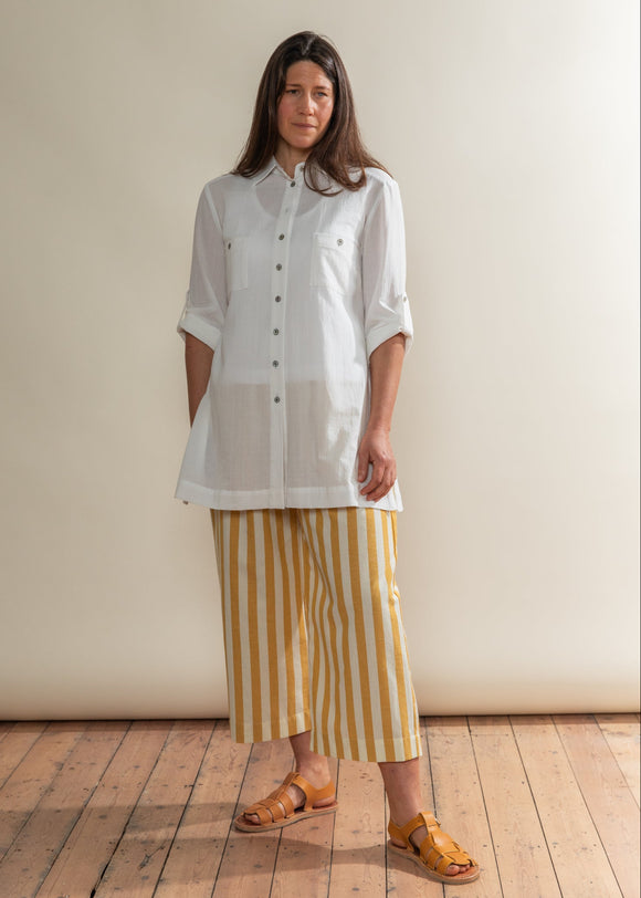 Woman wearing a white shirt and yellow striped pants standing against a plain wall.