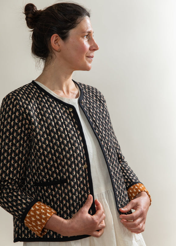 Woman wearing a patterned jacket over a white dress against a plain background