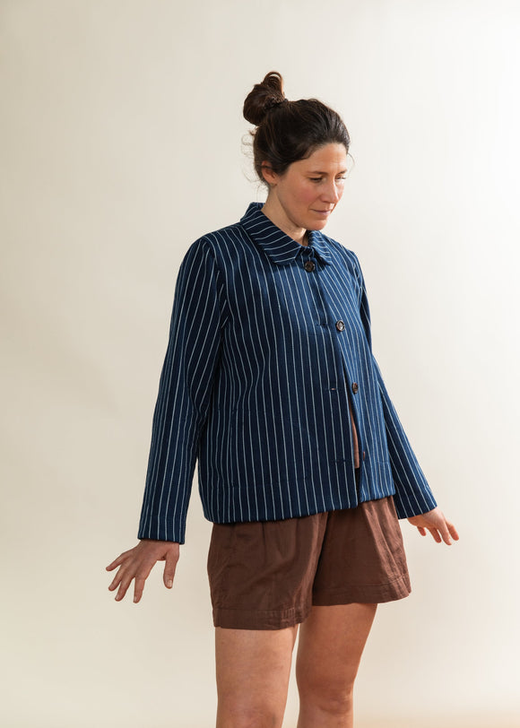 Woman wearing a blue pinstripe jacket and brown shorts against a white background