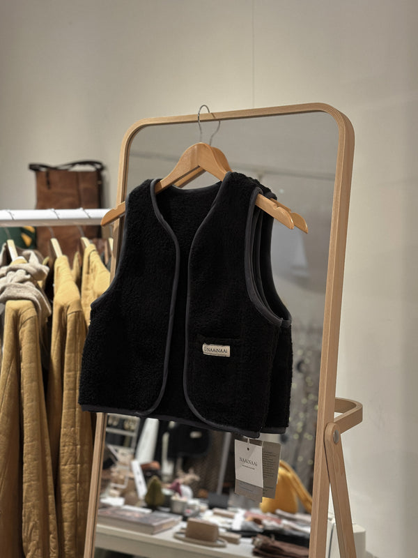 Black vest on a hanger in front of a mirror with clothing rack in the background