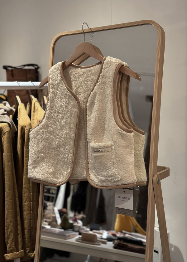 Beige textured vest on a hanger in front of a mirror with clothing rack in the background