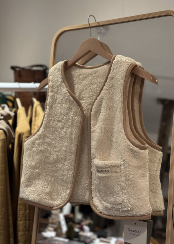 Beige fleece vest on a hanger with a blurred clothing store background