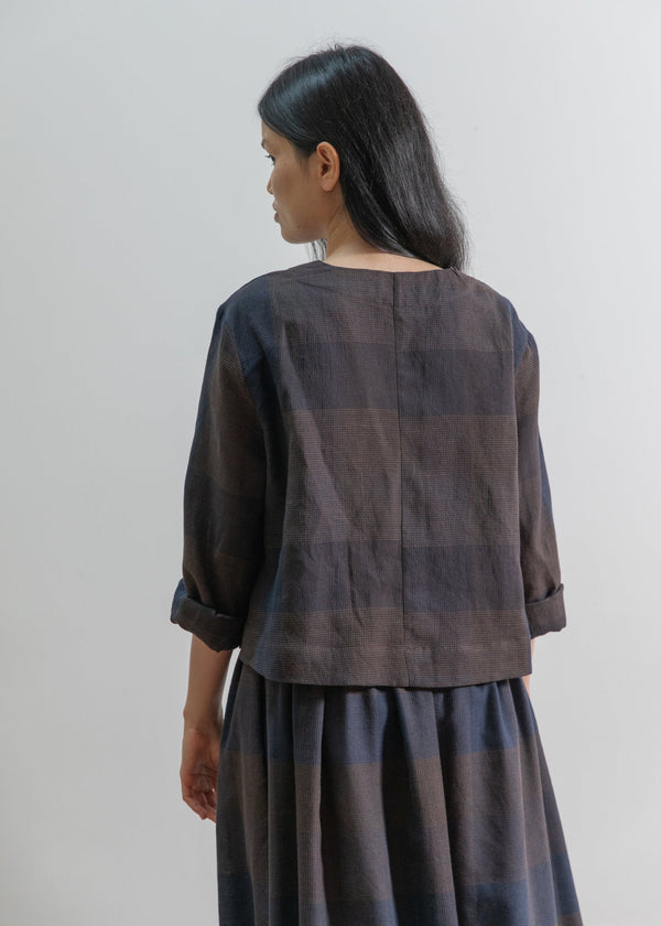 Woman wearing a dark brown checkered outfit against a plain background