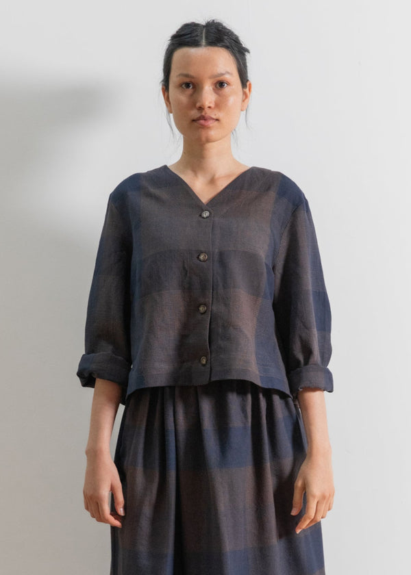 Person wearing a dark shirt and plaid skirt standing against a plain white wall.