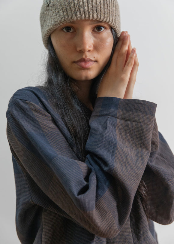 Person wearing a beige knit beanie and dark sweater against a plain background