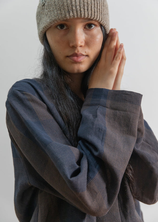 Person wearing a beige knit beanie and dark sweater against a plain background