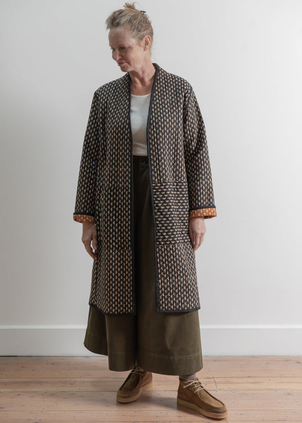 Person wearing a patterned coat and wide-leg pants on a plain background