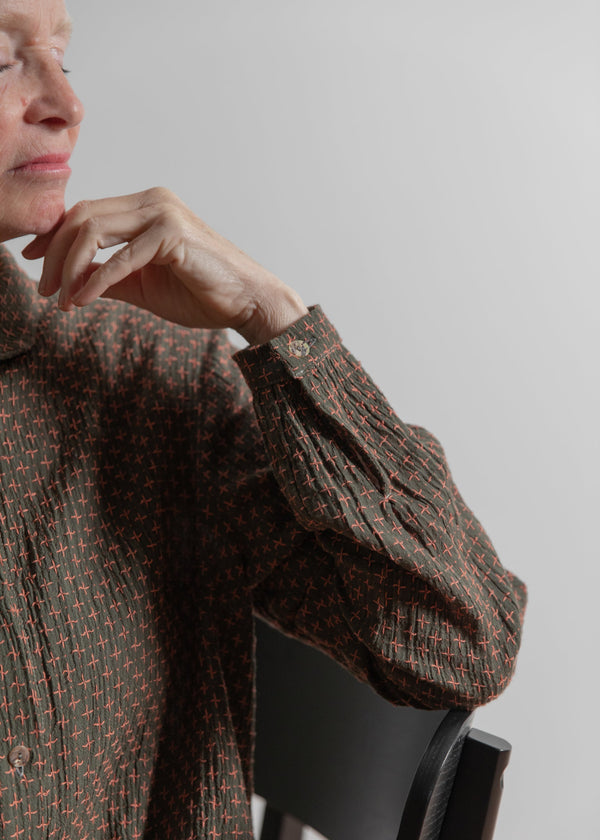 Person wearing a patterned brown sweater sitting on a chair against a plain background