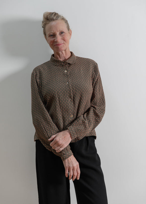 Person wearing a brown patterned shirt against a plain background