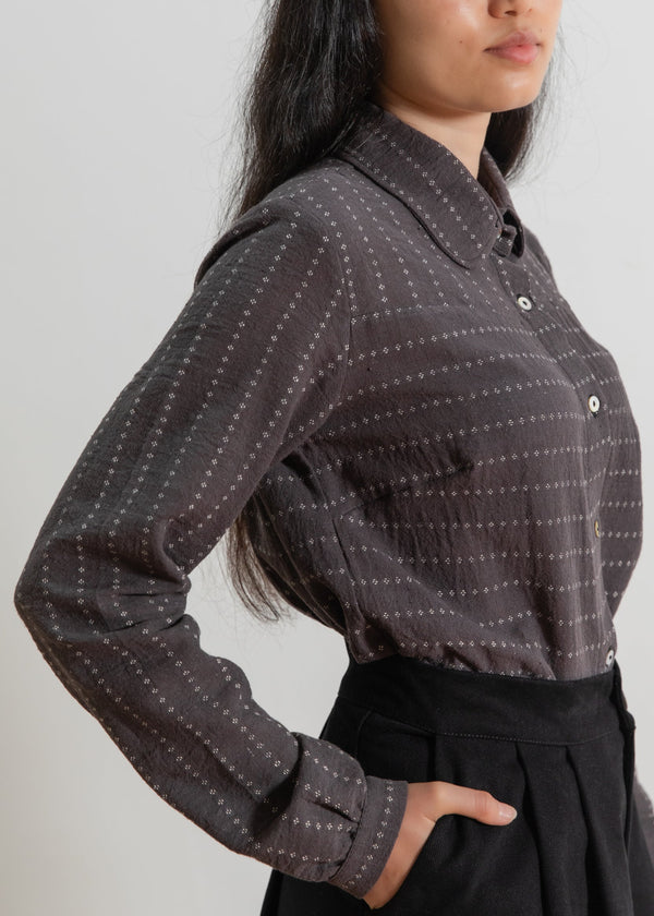 Person wearing a dark patterned shirt with a plain background