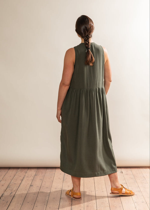 Woman wearing a green dress standing on a wooden floor with a white wall background