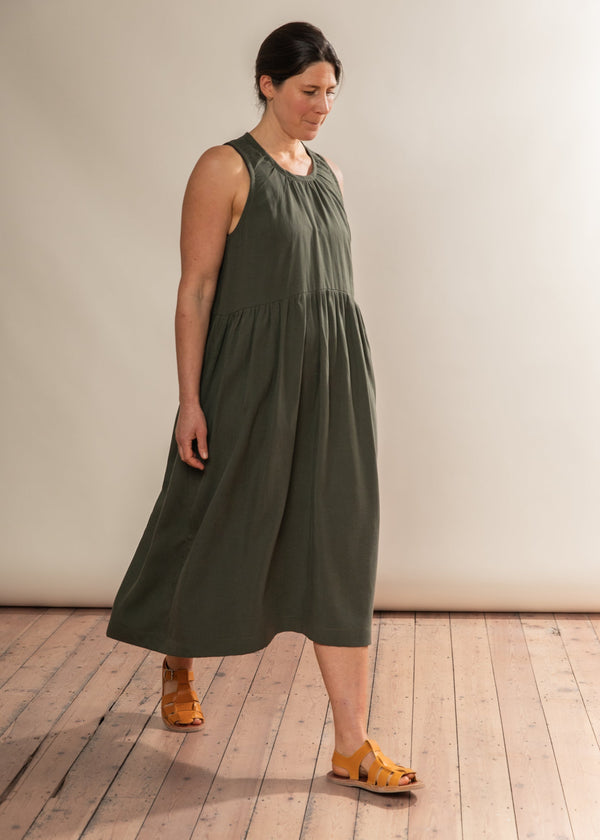 Woman wearing a green dress standing on a wooden floor with a white wall background