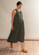Woman wearing a green dress standing on a wooden floor with a white wall background