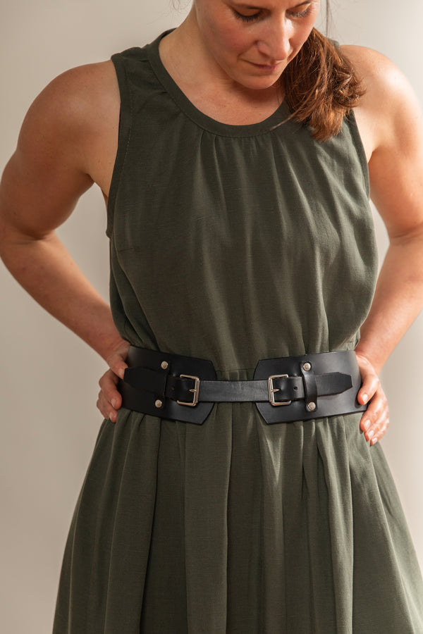 Woman wearing a green dress with a black belt against a plain background