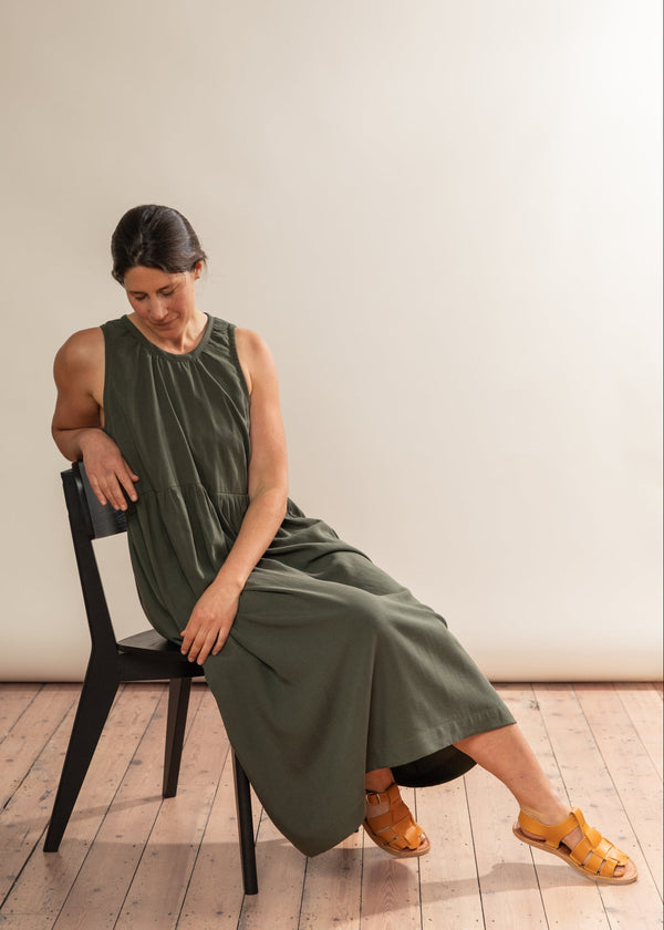 Woman in a green dress sitting on a black chair against a plain background