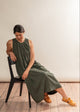 Woman in a green dress sitting on a black chair against a plain background